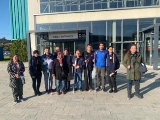 ESHOT Genel Müdürlüğü giriş kapısı önünde kadın erkek görme engelli ve gören bireylerden oluşan on bir kişilik bir grup kameraya doğru bakıyorlar.
