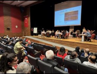 Selen Özel Bilgi Yarışmasının düzenlendiği salon. Sahnede yarışmacı gruplar, arkada projeksiyon perdesi ve koltuklarda oturan seyirciler görülüyor.